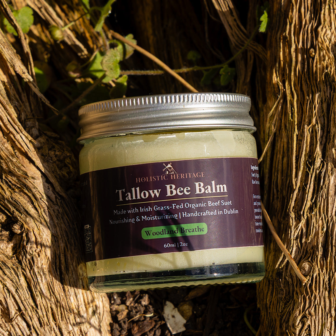 Jar of Holistic Heritage Woodland Breathe Tallow Bee Balm resting on textured tree bark surrounded by natural vines and greenery.